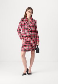 Rosa und schwarze Hahnentrittmuster-Blazer-Kleid mit doppelt geknöpften Knöpfen, Reverskragen und Fronttaschen; kombiniert mit schwarzen hohen Schuhen und einer kleinen Handtasche.