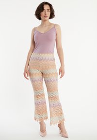 Lila tanktop gecombineerd met uitlopende broeken met een zigzagpatroon in pastelkleuren. De broeken hebben een gegolfde zoom en een textuurstof.