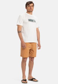 Bílá krátká bavlněná tričko s logem Quiksilver, v kombinaci s oranžovými šortkami a černými žabkami. Jednoduchý design, bavlněný materiál.