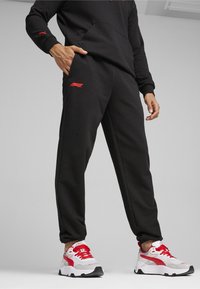 Sorte sweats med røde detaljer og F1-logo, parret med hvide og røde sneakers med grå detaljer og sorte såler. Glat stofstruktur.