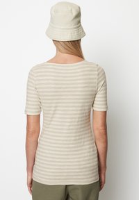 Béžové pruhované tričko s krátkými rukávy, vyrobené z měkké látky, s širokým výstřihem a přiléhavým siluetou, doplněné béžovým kloboukem typu bucket.