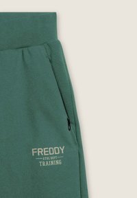 Pantaloni da tuta verdi con vita a costine, tasca con zip e stampa in beige chiaro "FREDDY ATHL DEPT TRAINING" sul davanti.