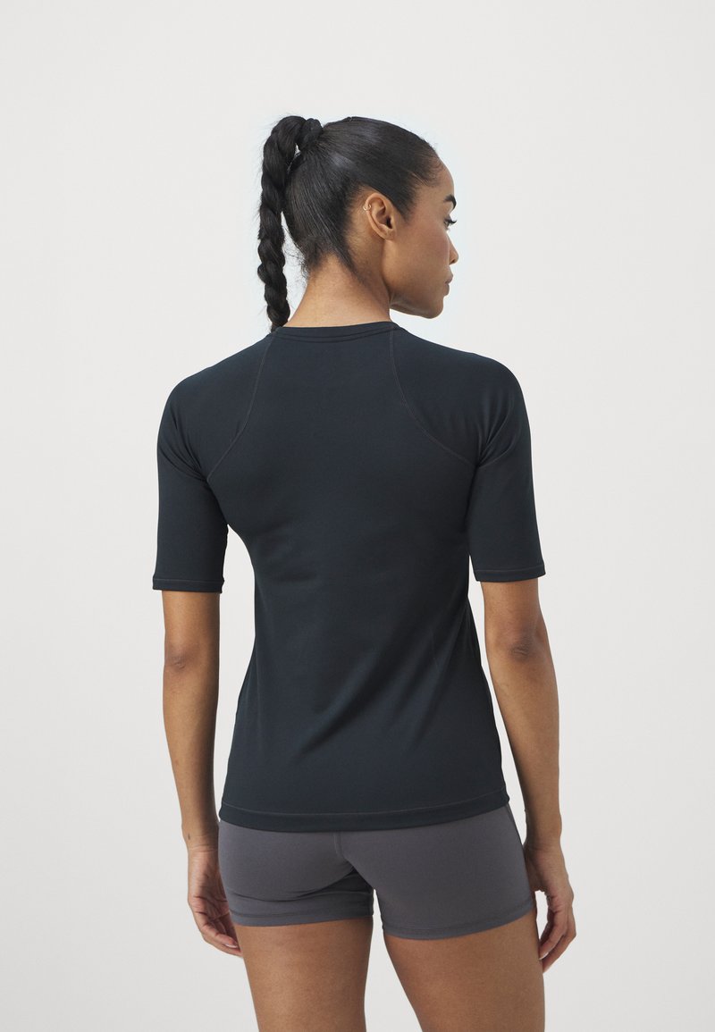 Camiseta atlética negra de manga corta con cuello redondo, con mangas raglán y textura suave. Usada con pantalones cortos atléticos grises.