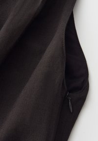 Gros plan sur un tissu sombre avec une fermeture éclair partiellement ouverte sur une couture pliée sur fond blanc.