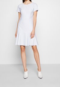 Lichtblauwe uitlopende jurk met korte mouwen, gestructureerde lijfje en een gladde textuur. Gecombineerd met witte hoge hakken.
