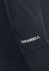 Czarna tkanina z białym logo "MERRELL" nadrukowanym na rękawie odzieży, prawdopodobnie kurtki lub bluzy.