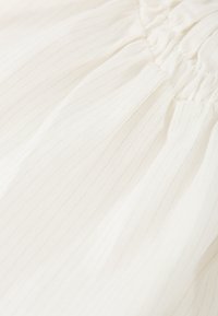Tejido blanco con sutiles rayas verticales y un leve brillo. Textura fruncida en la parte superior, superficie suave con un tacto agradable.