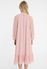 Helles rosa, langärmliges Kleid aus Chiffon mit rüschendem Saum, Schlüssel-Ausschnitt hinten und lockerer Silhouette. Strukturierter, fließender Stoff.