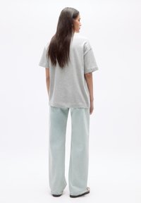 Un tricou gri cu mânecă scurtă, asortat cu blugi largi, de culoare albastru deschis, cu talie înaltă. Are o croială lejeră și o textură de țesătură moale.