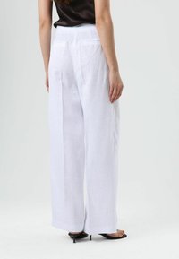 White linen wide-leg pants with a high waist, featuring side pockets and a clean finish, shown from the back with black heeled sandals.