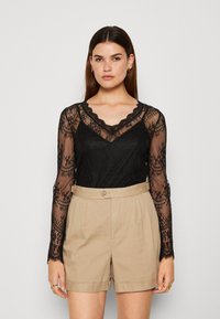 Černý dlouhý rukáv krajkový top s vlnitým výstřihem a květinovým vzorem, spárovaný s světle béžovými tailored šortkami s knoflíkovým zapínáním.