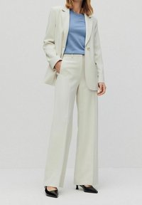 Krämfärgad kavaj och vida byxor i kombination med en blå T-shirt. Svarta spetsiga klackar. Slätt tyg och skräddarsydd design.