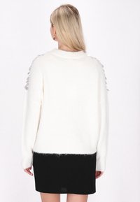 Weißer Strickpullover mit einer sanften Textur und lockerer Passform, verziert mit silbernen Pailletten an den Schultern. Kombiniert mit einem schwarzen Rock.