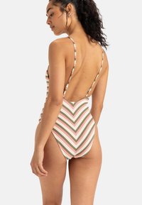 Eén delige zwemkleding van gestructureerde stof met verticale chevron-strepen in roze, groen en wit; lage rugontwerp met verstelbare bandjes.