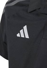 Polo noir en tissu texturé. Présente un logo brodé en trois rayures blanches en haut à gauche de la poitrine.