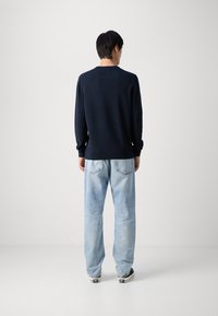 Marineblaues Strickpullover mit langen Ärmeln und rundem Halsausschnitt; kombiniert mit hellblauen, weit geschnittenen Jeans und schwarzen Sneakern. Schlichte, strukturierte Stoff.