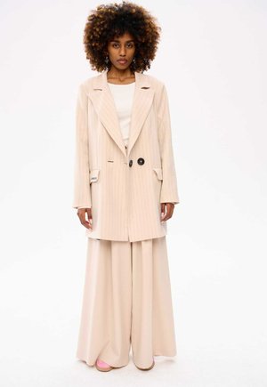 Beige pinstriped blazer with large black buttons, paired with wide-legged trousers in matching color. Smooth fabric with a tailored fit.