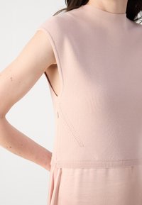 Světle růžové bezrukávové šaty s texturovanou pletenou horní částí, hladkým dolním materiálem a nenápadným bočním zipem.