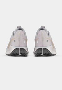 Ζευγάρι ανοιχτόχρωμων γκρι παπουτσιών τρεξίματος με μπεζ λεπτομέρειες, μαύρες σόλες με πέλματα, από πίσω σε λευκό φόντο.