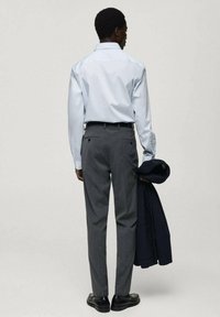 Cămașă bleu deschis cu butoni, pantaloni eleganți gri și pantofi negri. Sacoul este ținut în una dintre mâini. Are un design minimalist și o croială ajustată.