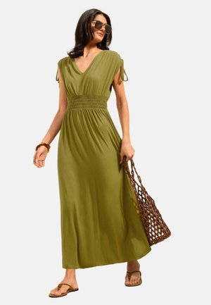 Nő olívazöld maxiruhában, húzott derékkal, barna fonott táskával, napszemüveggel és világosbarna szandállal.