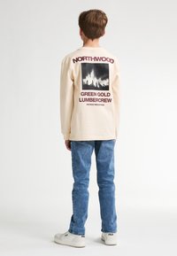 T-shirt a maniche lunghe color crema con un design grafico nero sul retro che riporta il testo "NORTHWOOD GREEN GOLD LUMBERCREW" in bordeaux.
