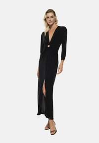 Abito lungo nero a maniche lunghe con profonda scollatura a V, frontale intrecciato con un'apertura circolare e uno spacco alto fino alla coscia. Tessuto liscio e silhouette aderente.