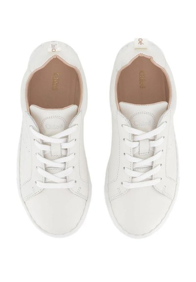 Une paire de baskets blanches en cuir avec lacets, dotées d'un intérieur beige et de la marque "Chloé" sur la semelle intérieure et le label de la languette.