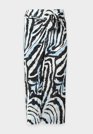 Woman wearing a long-sleeve midi dress with black, white, and light blue abstract zebra stripes, black heels, and holding a black handbag.