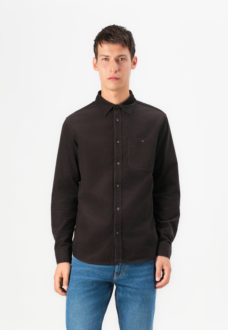Camisa negra de manga larga hecha de tela suave, con cuello de botón y un bolsillo en el pecho. Diseño simple con corte recto.