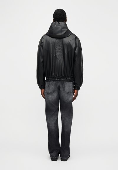 Fekete műbőr dzseki kapucnival, rugalmas derékrésszel és texturált díszítésekkel. Sötétszürke farmernadrággal párosítva. Minimalista dizájn.