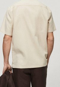 Beige kortarmig shirt met een rechte snit, een gladde textuur en subtiele stiksels op de schouders, gedragen met bruine broek.
