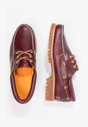 Burgundy leather shoes with brown rubber soles, round toe, white stitching, and gold eyelets. Interior features a yellow lining.