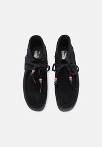 Sapatos pretos de camurça com perfil baixo, apresentando lados texturizados, atacadores pretos e contas decorativas nos atacadores para um pormenor adicional.