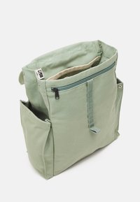 Groene canvas tas met een ritssluiting hoofdcompartiment, externe vakken en een eenvoudige rechthoekige vorm. Heeft een gestructureerd oppervlak en een verstelbare schouderband.