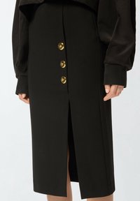 Gonna midi nera con spacco frontale e quattro bottoni dorati al centro, con una texture liscia e una vestibilità su misura.