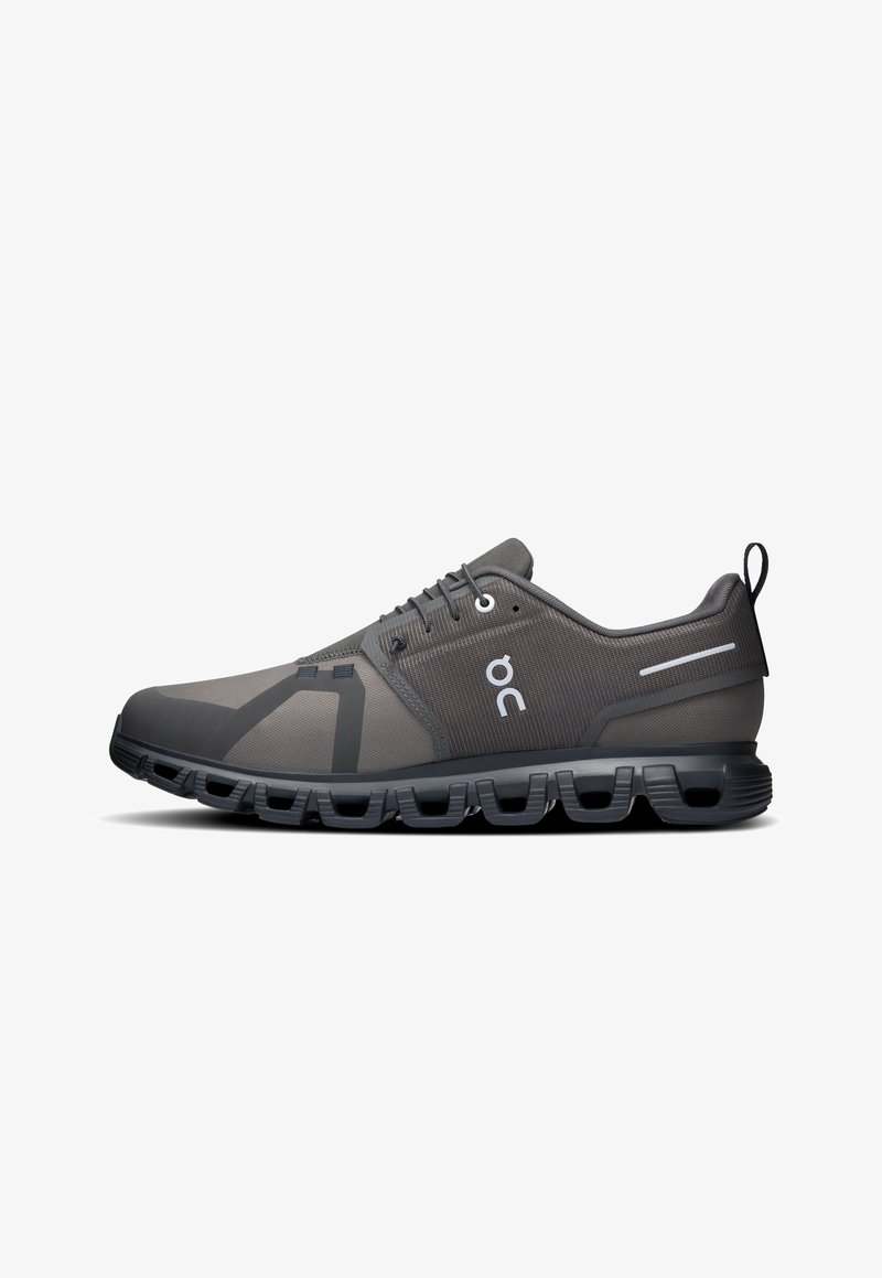 Scarpe sportive grigie con suola flessibile, tomaia in rete testurizzata, sovrapposizioni sintetiche e un sistema di allacciatura distintivo, con logo del marchio.