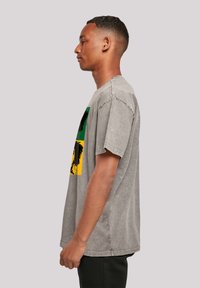 Grau Kurzarm-T-Shirt mit boxy Schnitt, das mehrfarbige Grafikdrucke von Palmen in Grün, Gelb und Schwarz zeigt.