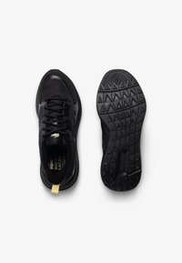 Czarne buty sportowe z siateczkowej tkaniny i gumową podeszwą. Posiadają żółtą pętelkę na pięcie oraz teksturowaną czarną podeszwę zewnętrzną z trójkątnymi wzorami.