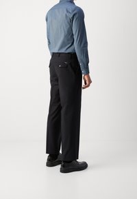 Jasnoniebieska koszula dżinsowa z zapinanymi na guziki mankietami, w połączeniu z czarnymi spodniami z dwoma tylnymi kieszeniami i gładką teksturą. Całość dopełniają czarne buty.