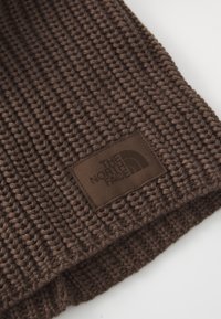 Brązowa dzianina prążkowana z naszywaną prostokątną naszkicowaną metką, na której znajduje się logo "The North Face" w pasujących odcieniach brązu.