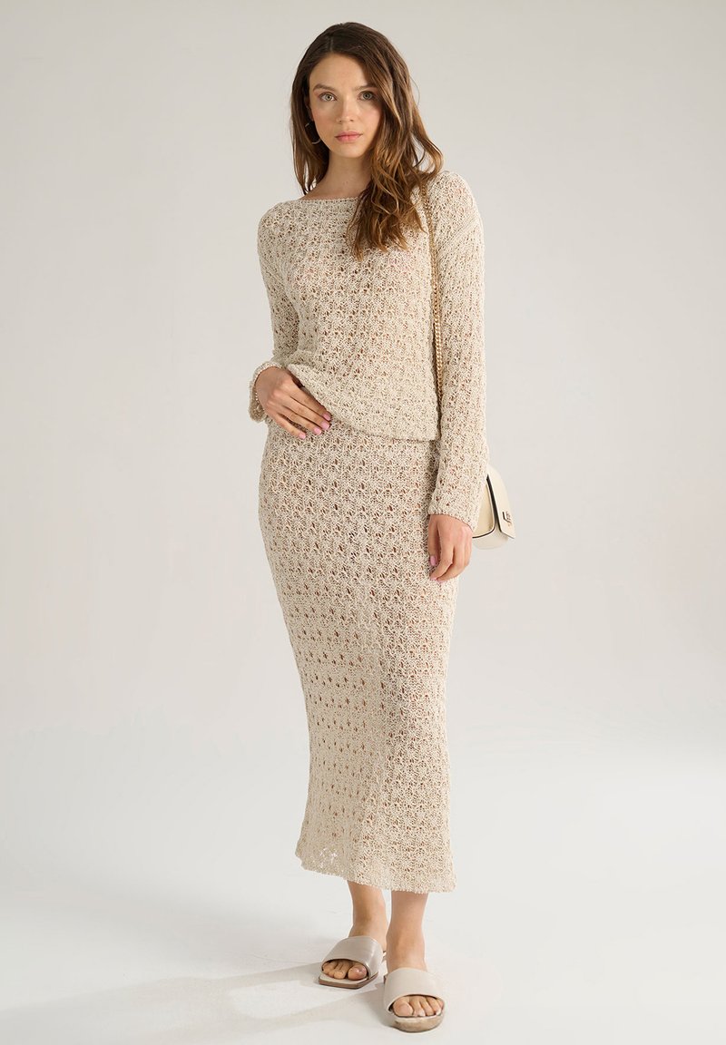 Set di maglia a due pezzi in beige chiaro, composto da un top a maniche lunghe e una gonna midi con motivo traforato; abbinato a scarpe slip-on beige.