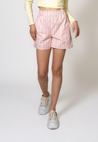 Rosa stripete shorts med elastisk midjebånd, med vertikale striper i pastellfarger. Båret med hvite plattform sneakers.