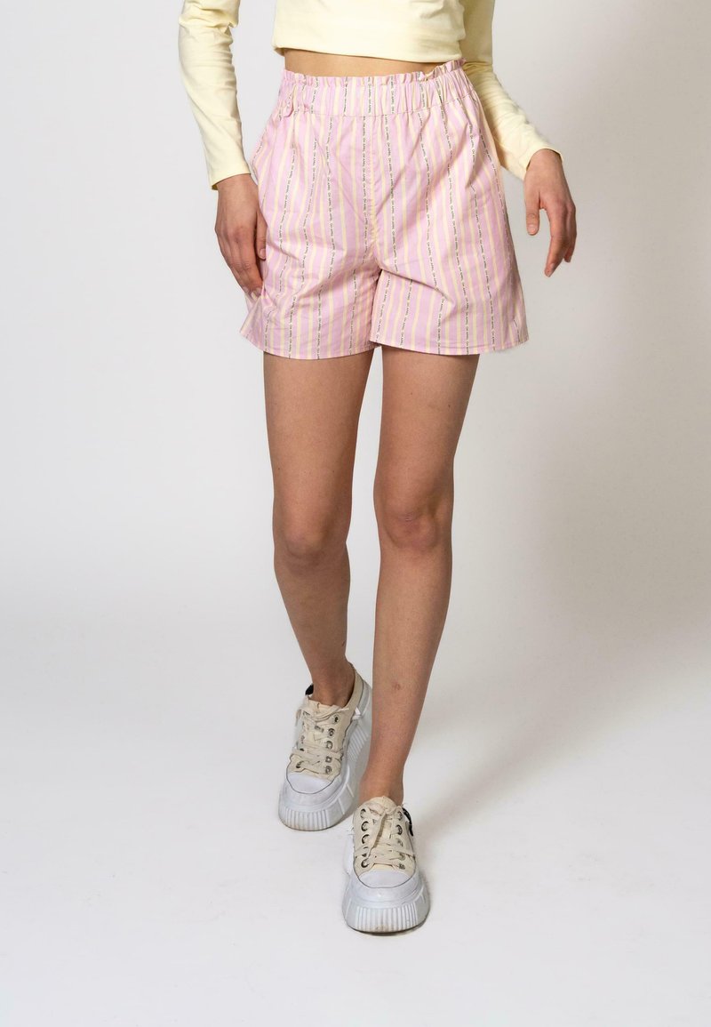 Rosa stripete shorts med elastisk midjebånd, med vertikale striper i pastellfarger. Båret med hvite plattform sneakers.