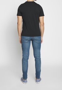 Camiseta negra de manga corta combinada con jeans azules. La camiseta tiene un diseño simple con un cuello redondo, forma ajustada y sin patrones visibles.