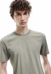 Olivegrøn t-shirt i bomuld med korte ærmer, rund halsudskæring og glat tekstur. Minimalistisk design, ingen synlige mønstre eller logoer.