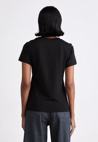Black cotton t-shirt with short sleeves, crew neck, and a smooth texture, displayed from the back, paired with dark denim pants.