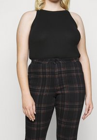 Marta musta ilmanhihoilla musta paita, jossa on ribbiohennus, yhdistettyinä mustiin ruudullisiin housuihin, joissa on oranssia ja harmaata sävyä sekä kapea vyötärö.