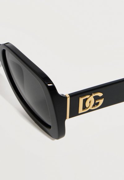 Μαύρα ορθογώνια γυαλιά ηλίου με χοντρά πλαίσια και χρυστό διαπλεκόμενο λογότυπο DG στο πλαϊνό μπράτσο, πάνω σε λευκό φόντο.