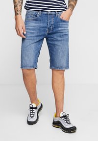 Jeansshorts i ljusblått, knälängd med en klassisk femficksdesign. Bärs med svartvita sportskor med gula detaljer.